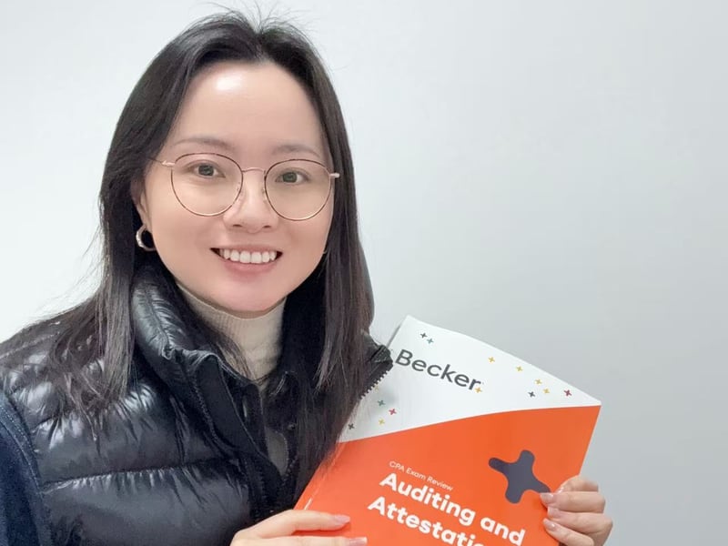 Kate 伊同学正面合影：戴眼镜羽绒马甲手捧 Becker AUD Auditing and Attestation 教材